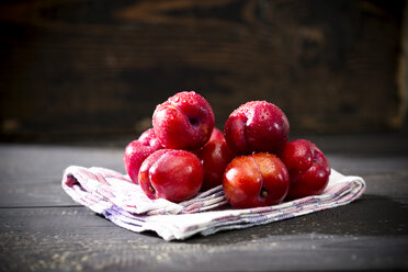 Stapel chinesischer Pflaumen (Prunus salicina) auf Küchenhandtuch und dunklem Holztisch - MAEF008220