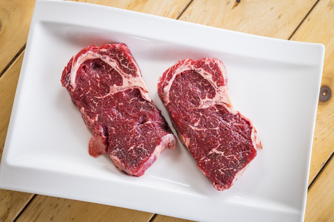 Two raw beef steaks on white serving plate stock photo