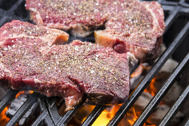 Beef steaks grilling over charcoal on barbecue grill - ABAF001276