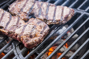 Beef steaks grilling over charcoal on barbecue grill - ABAF001277