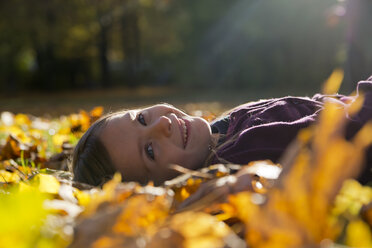 Porträt eines lächelnden kleinen Mädchens, das auf Herbstblättern im Park liegt - SARF000401