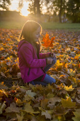Little girl crouching in between autumn leaves in park - SARF000370
