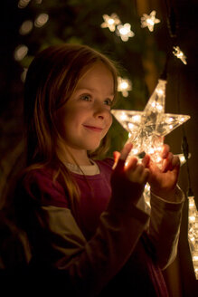 Porträt eines lächelnden kleinen Mädchens, das einen beleuchteten Stern aus Lichterketten hält - SARF000373