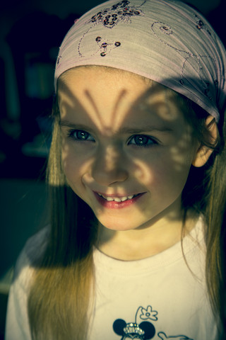 Portrait of little girl with butterfly-shaped shadow in her face stock photo