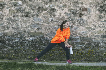 Junge Joggerin beim Stretching vor einer Steinmauer - EBSF000109