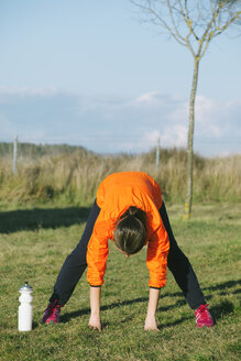 Junge Joggerin beim Stretching auf einer Wiese - EBSF000111