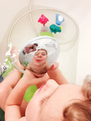 Junge betrachtet sein Spiegelbild auf dem Duschkopf, lizenzfreies Stockfoto