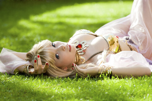 Woman wearing belly dance costume lying in grass - AFF000039