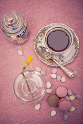 Gedeckter Tisch mit Tasse Tee, Narzisse (Narcissus pseudonarcissus), Macarons und einem Glas Süßigkeiten, Blick von oben - VTF000166