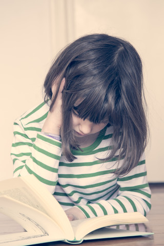 Kleines Mädchen liest Buch zu Hause, lizenzfreies Stockfoto