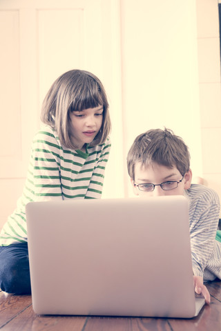 Brother and sister using laptop at home stock photo
