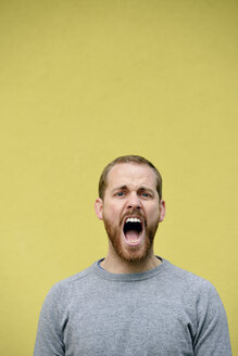 Portrait of screaming young man in front of yellow background - BR000170