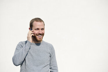 Porträt eines jungen Mannes, der mit einem Smartphone vor einem weißen Hintergrund telefoniert - BR000184