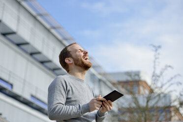 Porträt eines lachenden jungen Mannes mit Mini-Tablet - BR000179