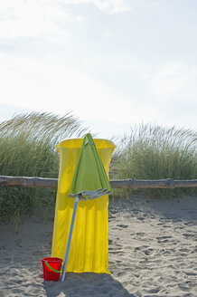 Italy, Adria, yellow air bed, basket and beach umbrella leaning at beach dunes - ASF005282