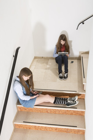Two teenage girls sitting on stairs using smartphone and digital tablet stock photo