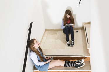 Two teenage girls sitting on stairs using smartphone and digital tablet - MAEF008277