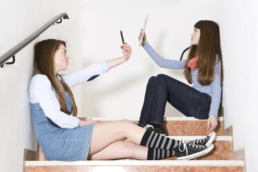 Zwei Mädchen im Teenageralter sitzen auf einer Treppe und benutzen ein Smartphone und ein digitales Tablet - MAEF008282