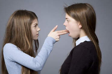 Teenage girl making gun sign against her sister - MAEF008248