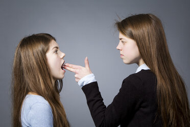 Teenage girl making gun sign against her sister - MAEF008249