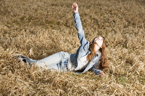 Porträt eines Teenagers mit ausgestrecktem Arm auf einem Feld liegend - MAEF008269