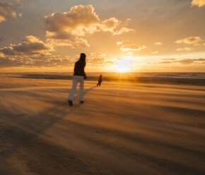 Denmark, Jutland, Lokken, mother trying to catch her child on stormy beach at sunset - JBF000071