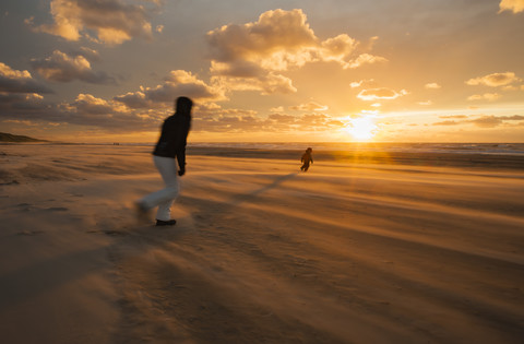 Denmark, Jutland, Lokken, mother trying to catch her child on stormy beach at sunset stock photo