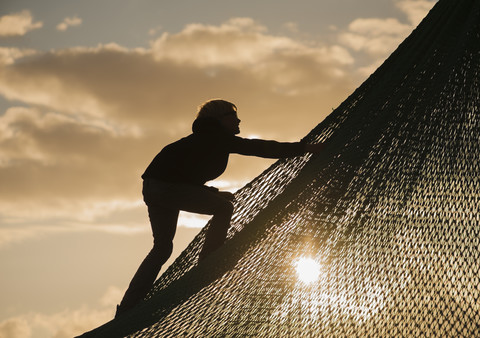 Denmark, Jutland, Vejers, climbing boy at sunset stock photo