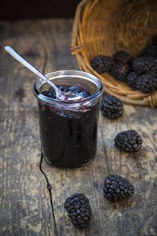 Korb mit Brombeeren (Rubus sectio Rubus) und Einmachglas mit Brombeergelee auf Holztisch, lizenzfreies Stockfoto