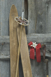 Alte Skier, Skistock, rote Schleife mit Edelweiss (Leontopodium alpinum) an Holzwand gelehnt - ASF005288