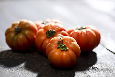 Fünf Ochsenherz-Tomaten auf dunklem Holz, Nahaufnahme - MAEF008198