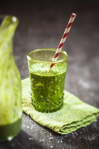 Glas Spinat-Smoothie mit Kokosnussmilch, Zitronen- und Orangensaft und Banane auf Serviette und Holztisch, lizenzfreies Stockfoto