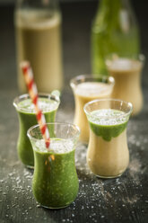 Glasses of spinach smoothie and mango smoothie with desiccated coconut on wooden table - SBDF000652