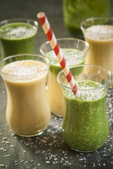 Glasses of spinach smoothie and mango smoothie with desiccated coconut on wooden table - SBDF000653