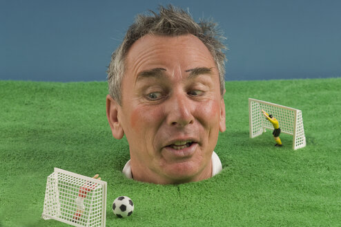 Man watching soccer game with head out of football pitch, studio shot - ASF005296