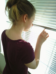 Young woman looking through blinds out of the window, Germany - UWF000046