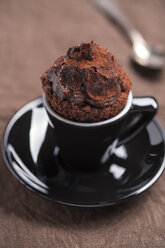 Schwarze Tasse mit Schokoladenkuchen und einem Teelöffel auf braunem Tuch - MYF000240