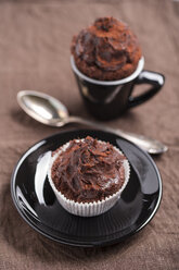 Black cup and a paper cup of chocolate cup cake and a tea spoon on brown cloth - MYF000247