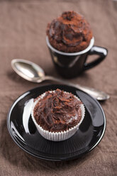 Schwarze Tasse und ein Papierbecher mit Schokoladenkuchen und ein Teelöffel auf braunem Tuch - MYF000247