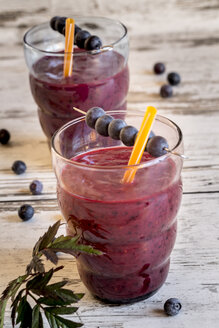 Zwei Gläser mit Waldbeeren-Smoothie und Blaubeeren auf dem Holztisch - SARF000393