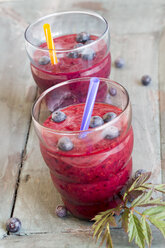 Two glasses of wild berry smoothie and blueberries on wooden table - SARF000394