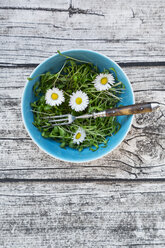 Bowl of garden cress salad and daisies (Bellis perennis) on grey wooden table, view from above - LVF000904