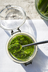 Preserving jar of wild garlic pesto on napkin and grey wooden table, view from above - LVF000912