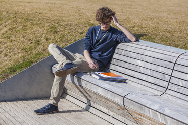 Germany, Baden-Wurttemberg, Teenage boy sitting on bench, learning - WDF002413