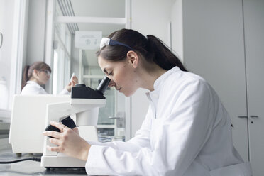 Porträt einer jungen Studentin, die ein Mikroskop im Labor benutzt - SGF000474
