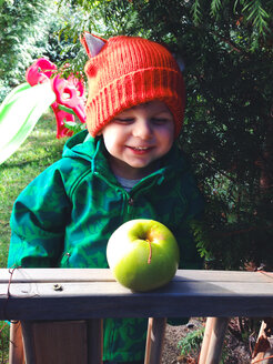 little boy with red hat laughing and looking at apple - AFF000047