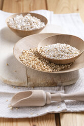 Bowls of puffed buckwheat, amaranth and quinoa on wooden board and kitchen towel - MYF000261