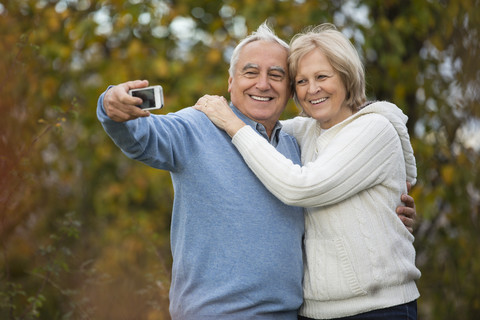 Porträt eines glücklichen älteren Paares, das sich mit einem Smartphone selbst porträtiert, lizenzfreies Stockfoto