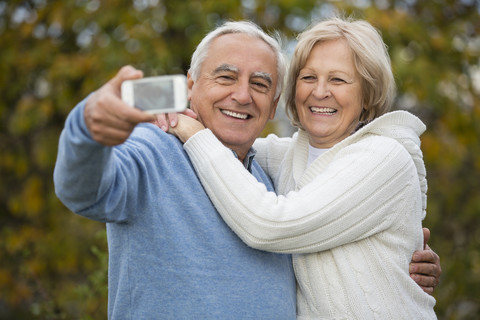 Porträt eines lächelnden älteren Paares, das sich mit einem Smartphone selbst porträtiert, lizenzfreies Stockfoto