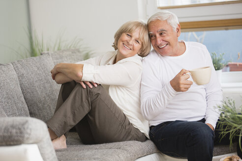 Lächelndes Seniorenpaar nebeneinander auf dem Sofa im Wohnzimmer - WESTF019241